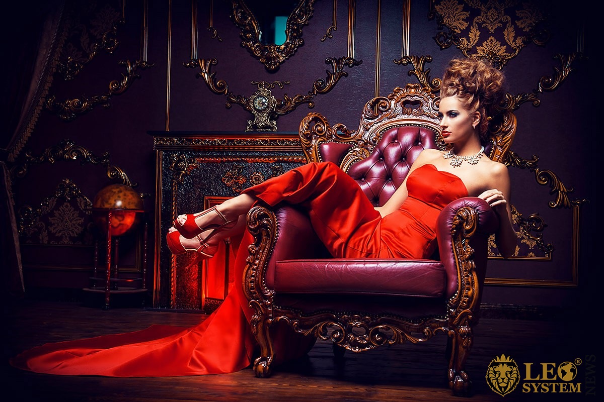 Bright woman sitting on an expensive armchair in a red dress