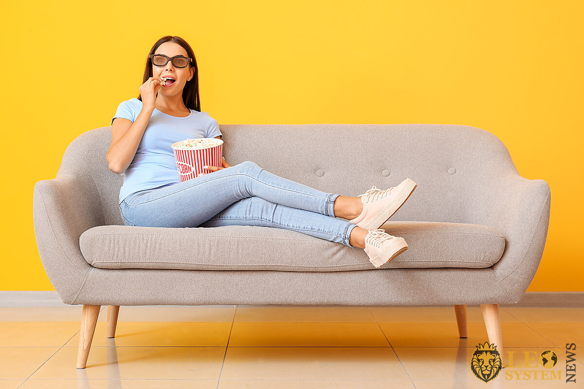 Surprised woman sitting on sofa and eating popcorn