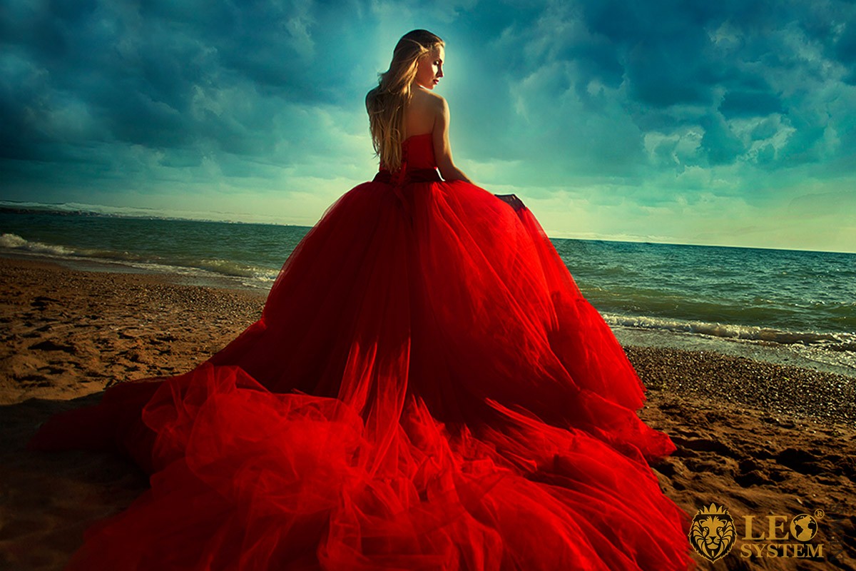 Photo of a girl in a lush red dress on the background of the coast
